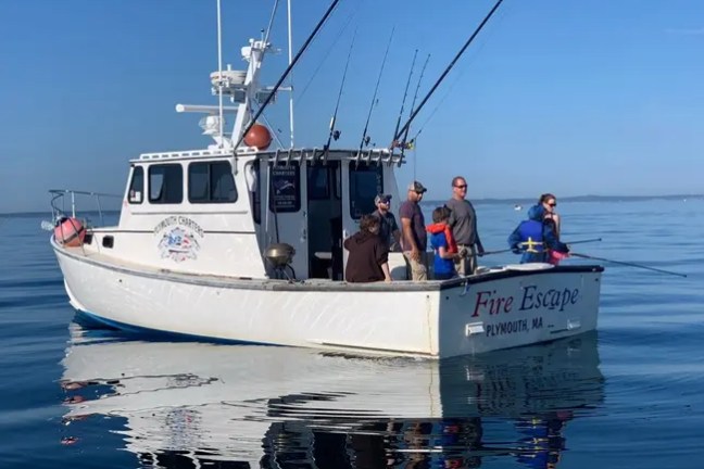 Group on a boat named 'Fire Escape' fishing on calm water with a clear sky.