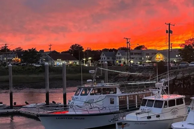 Boats docked at a harbor with a vibrant red and orange sunset sky.