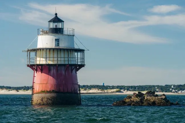 Lighthouse on red and white base surrounded by ocean under blue sky.