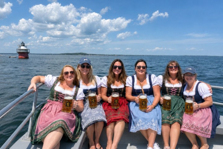 Six women in traditional dresses holding beer mugs on a boat.
